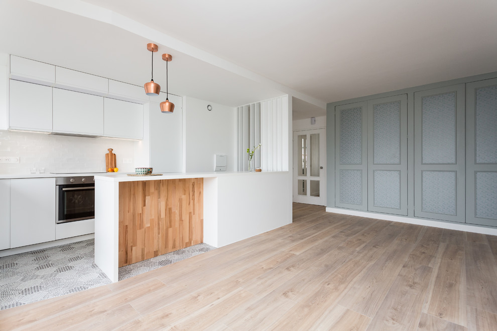 Design ideas for a small contemporary galley open plan kitchen in Paris with a single-bowl sink, flat-panel cabinets, white cabinets, laminate countertops, white splashback, ceramic splashback, black appliances, ceramic flooring, an island, multi-coloured floors and white worktops.