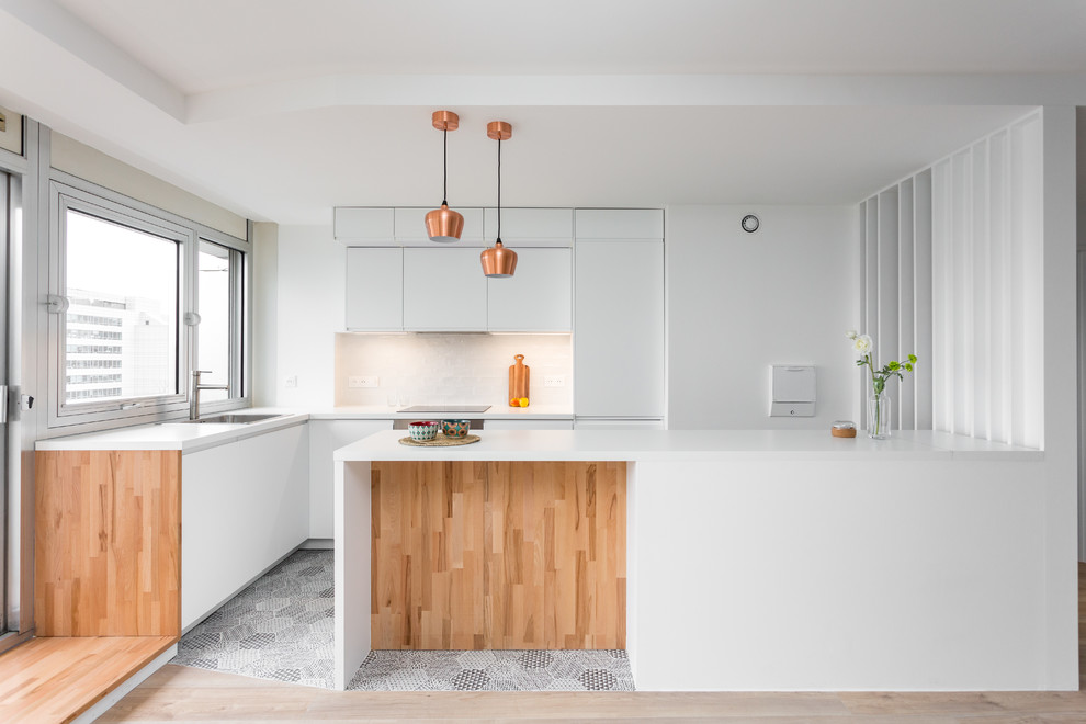 Contemporary l-shaped kitchen in Paris with a built-in sink, flat-panel cabinets, white cabinets, integrated appliances, a breakfast bar, grey floors and white worktops.