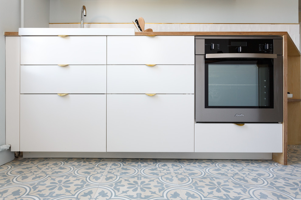 パリにあるお手頃価格の中くらいな北欧スタイルのおしゃれなキッチン (シングルシンク、フラットパネル扉のキャビネット、白いキャビネット、木材カウンター、白いキッチンパネル、セラミックタイルのキッチンパネル、シルバーの調理設備、セメントタイルの床、アイランドなし、青い床、ベージュのキッチンカウンター) の写真