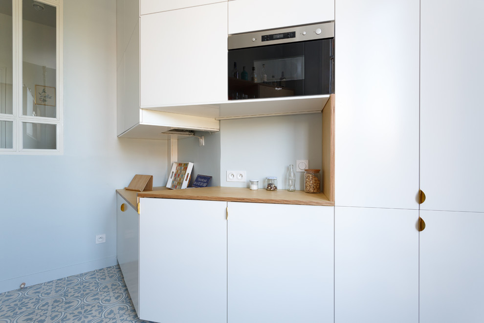 This is an example of a medium sized scandi galley enclosed kitchen in Paris with a single-bowl sink, flat-panel cabinets, white cabinets, wood worktops, white splashback, ceramic splashback, stainless steel appliances, cement flooring, no island, blue floors and beige worktops.