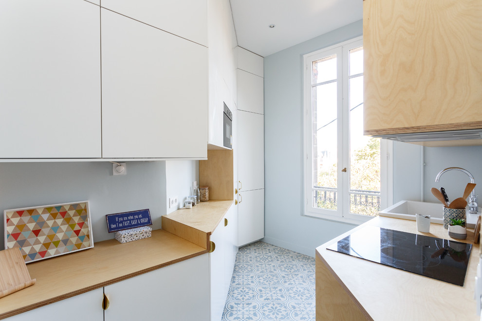 パリにあるお手頃価格の中くらいな北欧スタイルのおしゃれなキッチン (シングルシンク、フラットパネル扉のキャビネット、白いキャビネット、木材カウンター、白いキッチンパネル、セラミックタイルのキッチンパネル、シルバーの調理設備、セメントタイルの床、アイランドなし、青い床、ベージュのキッチンカウンター) の写真