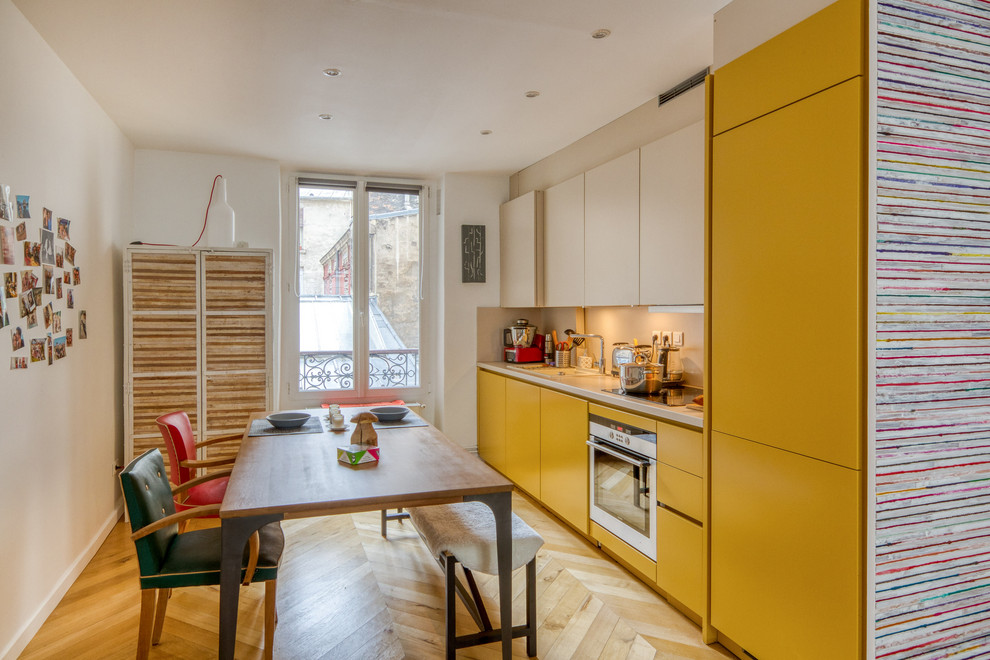 パリにあるコンテンポラリースタイルのおしゃれなキッチン (シングルシンク、フラットパネル扉のキャビネット、黄色いキャビネット、ベージュキッチンパネル、シルバーの調理設備、淡色無垢フローリング、アイランドなし、ベージュの床、ベージュのキッチンカウンター) の写真