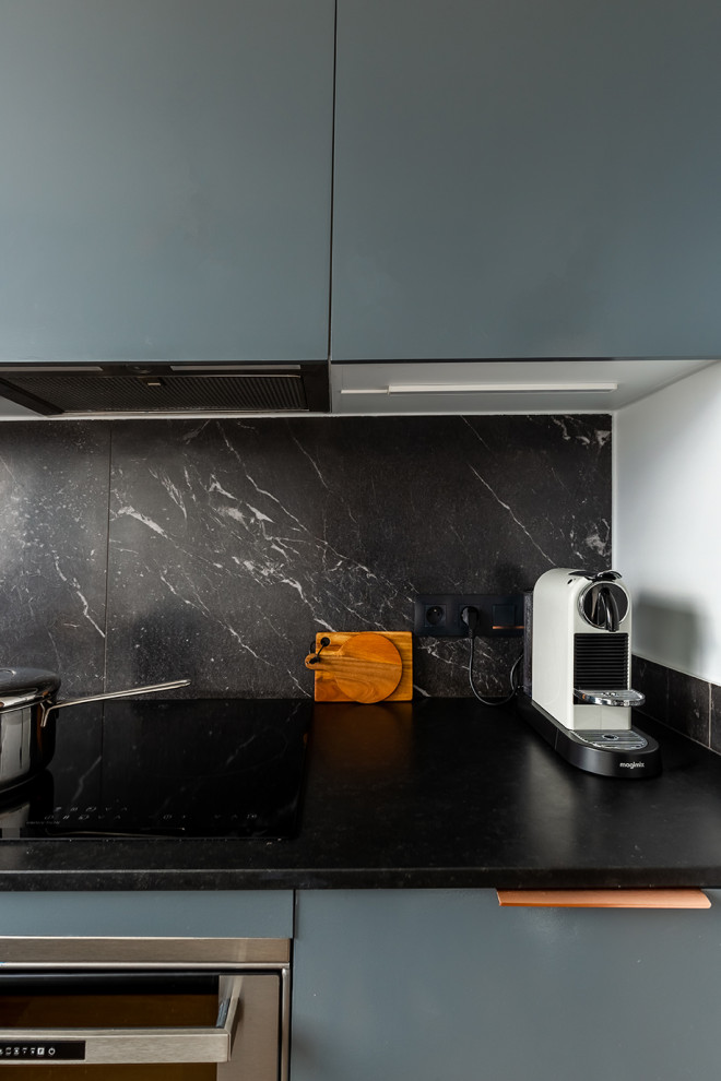 Immagine di una piccola cucina a L design chiusa con lavello sottopiano, ante a filo, ante blu, top in granito, paraspruzzi nero, paraspruzzi con piastrelle in ceramica, elettrodomestici neri e top nero