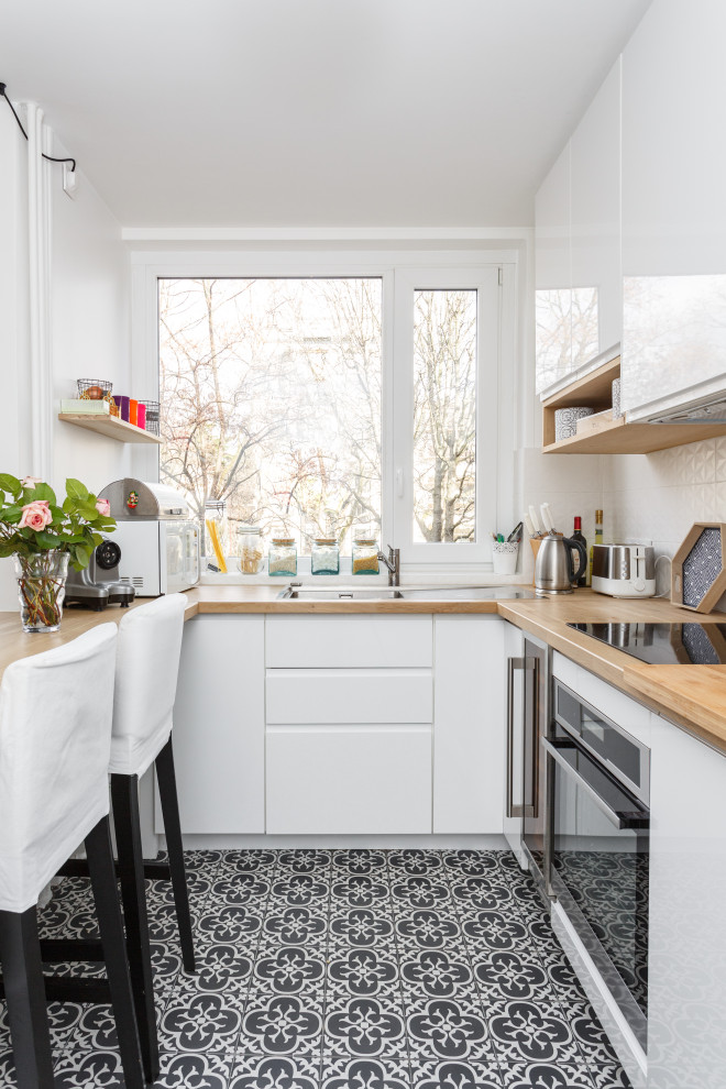 Minimalistisk inredning av ett u-kök, med släta luckor, vita skåp, träbänkskiva, vitt stänkskydd och flerfärgat golv