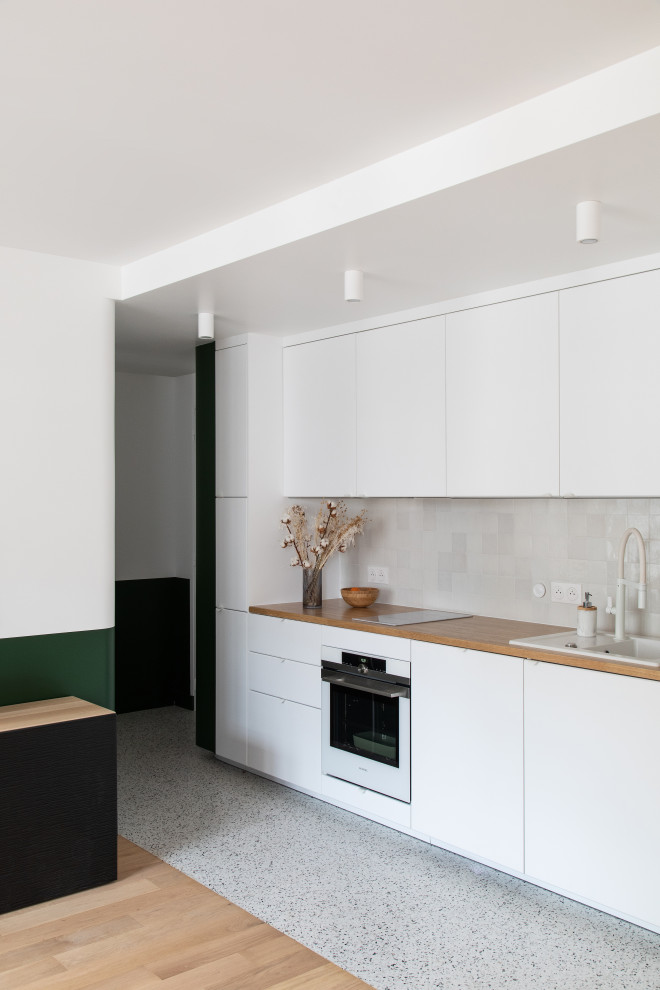 Inredning av ett modernt litet beige linjärt beige kök och matrum, med en enkel diskho, luckor med profilerade fronter, vita skåp, träbänkskiva, vitt stänkskydd, stänkskydd i keramik, vita vitvaror, terrazzogolv och flerfärgat golv