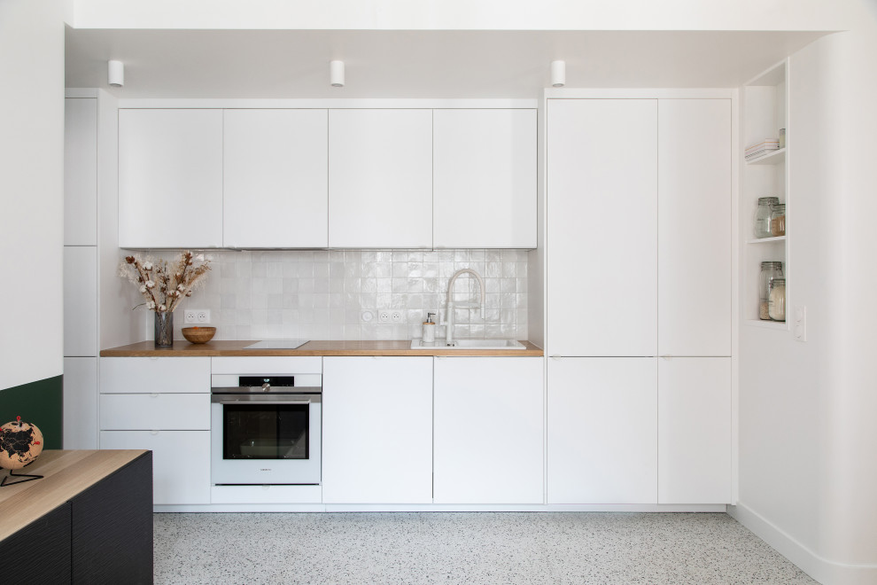 Idéer för att renovera ett litet funkis beige linjärt beige kök och matrum, med en enkel diskho, luckor med profilerade fronter, vita skåp, träbänkskiva, vitt stänkskydd, stänkskydd i keramik, vita vitvaror, terrazzogolv och flerfärgat golv