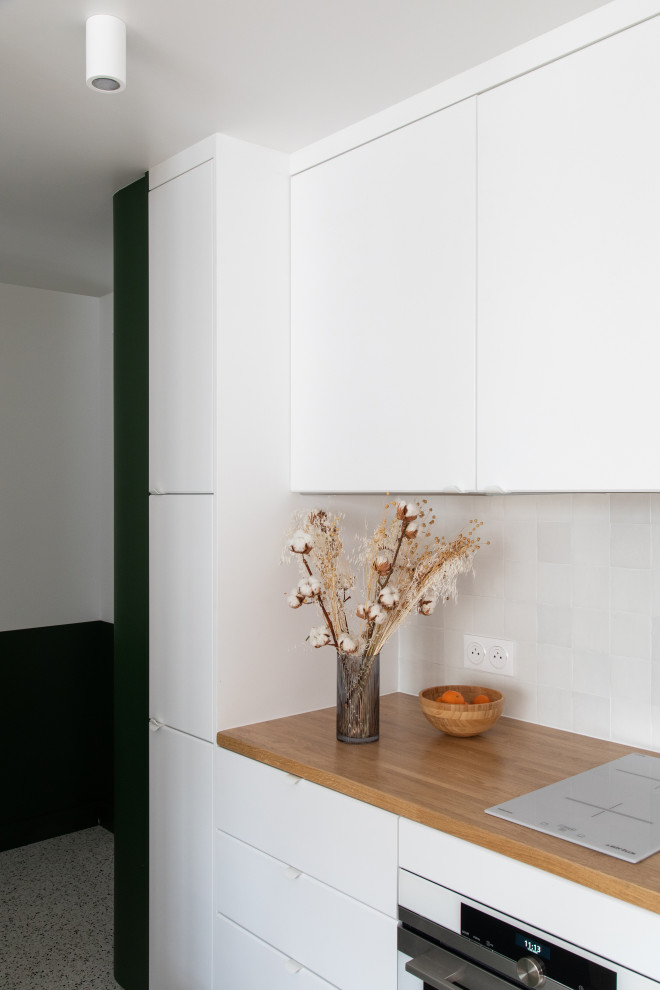パリにあるお手頃価格の小さなコンテンポラリースタイルのおしゃれなキッチン (シングルシンク、インセット扉のキャビネット、白いキャビネット、木材カウンター、白いキッチンパネル、セラミックタイルのキッチンパネル、白い調理設備、テラゾーの床、マルチカラーの床、ベージュのキッチンカウンター) の写真