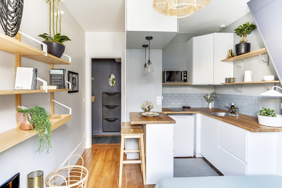 Inspiration for a medium sized contemporary u-shaped open plan kitchen in Paris with flat-panel cabinets, white cabinets, wood worktops, grey splashback, brown floors, brown worktops, a submerged sink, ceramic splashback, stainless steel appliances, light hardwood flooring and no island.