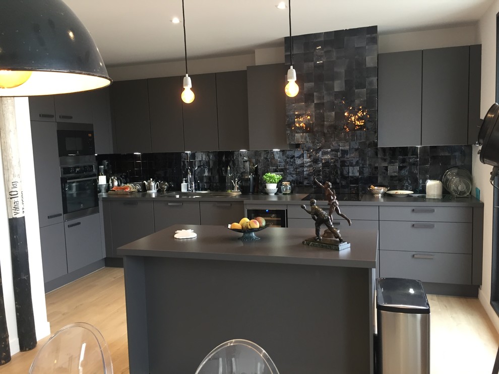 Large urban grey and black galley kitchen/diner in Nice with a submerged sink, beaded cabinets, grey cabinets, laminate countertops, black splashback, terracotta splashback, stainless steel appliances, light hardwood flooring, an island and beige floors.