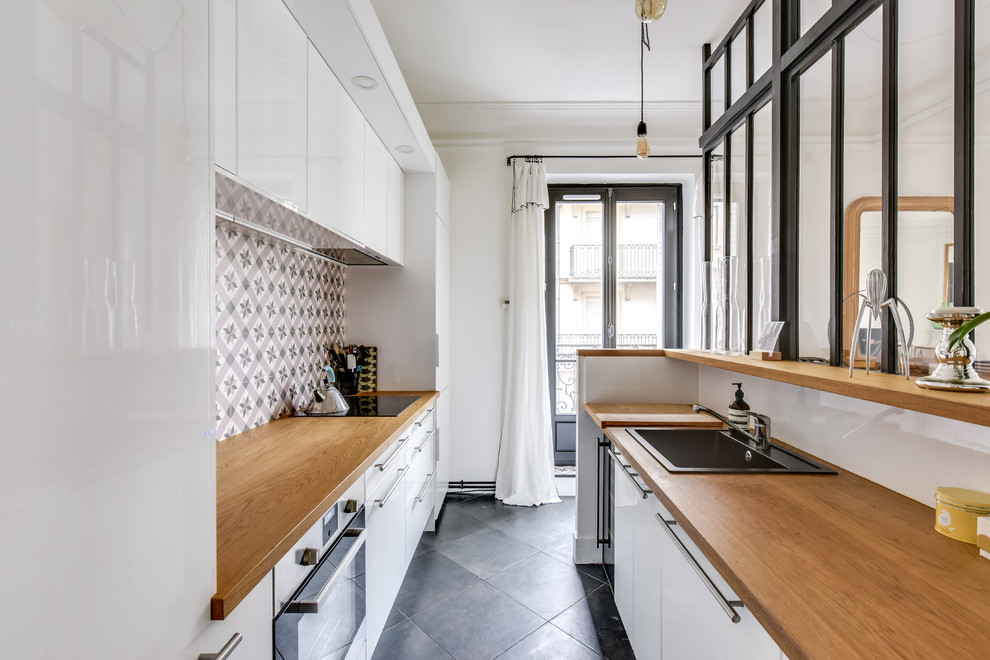 パリにある高級な中くらいなコンテンポラリースタイルのおしゃれなキッチン (白いキャビネット、木材カウンター、シルバーの調理設備、グレーの床、ドロップインシンク、フラットパネル扉のキャビネット、マルチカラーのキッチンパネル、セメントタイルのキッチンパネル、アイランドなし、セラミックタイルの床) の写真