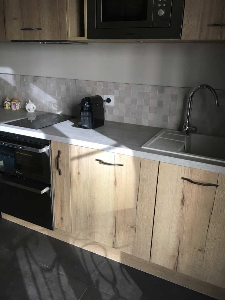 This is an example of a small traditional single-wall open plan kitchen in Paris with a submerged sink, beaded cabinets, light wood cabinets, laminate countertops, grey splashback, stone tiled splashback, stainless steel appliances, ceramic flooring, an island, grey floors and grey worktops.