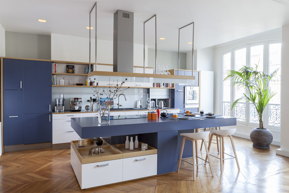 Example of a trendy medium tone wood floor kitchen design in Paris with flat-panel cabinets, white cabinets, white backsplash, glass sheet backsplash and an island