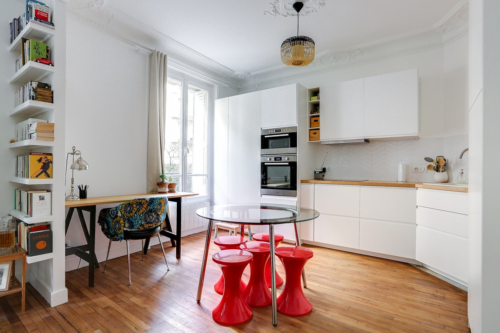 パリにあるエクレクティックスタイルのおしゃれなキッチン (ドロップインシンク、フラットパネル扉のキャビネット、白いキャビネット、木材カウンター、白いキッチンパネル、シルバーの調理設備、無垢フローリング、アイランドなし、茶色い床) の写真