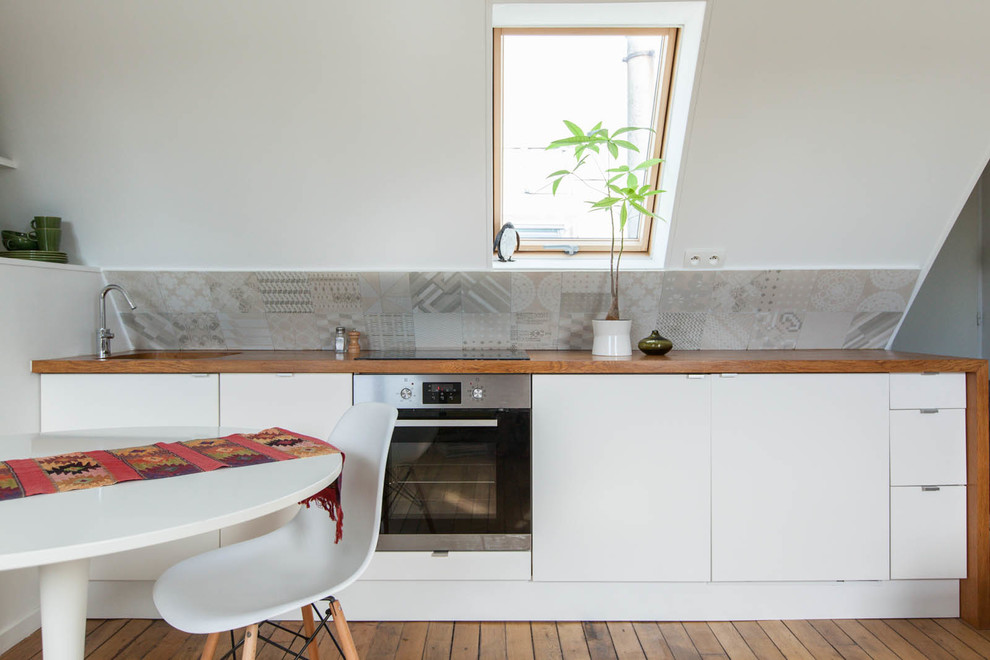 Cette image montre une petite cuisine américaine linéaire design avec un placard à porte plane, des portes de placard blanches, une crédence grise, un évier encastré, un sol en bois brun et aucun îlot.