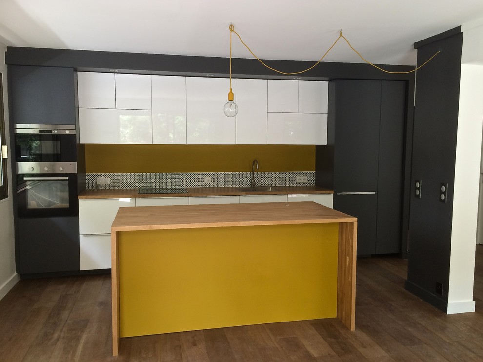 Photo of a contemporary galley kitchen/diner in Paris with a submerged sink, white cabinets, wood worktops, yellow splashback, ceramic splashback, integrated appliances, light hardwood flooring and an island.