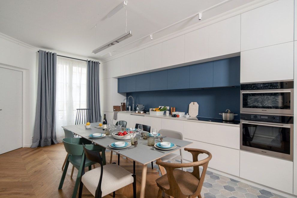 Einzeilige Moderne Küche ohne Insel mit flächenbündigen Schrankfronten, weißen Schränken, Küchenrückwand in Blau, Küchengeräten aus Edelstahl, buntem Boden und weißer Arbeitsplatte in Paris