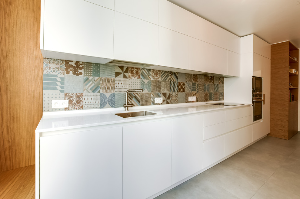 Diseño de cocina lineal contemporánea de tamaño medio sin isla con fregadero bajoencimera, puertas de armario blancas, encimera de cuarcita, salpicadero multicolor, electrodomésticos negros y suelo gris