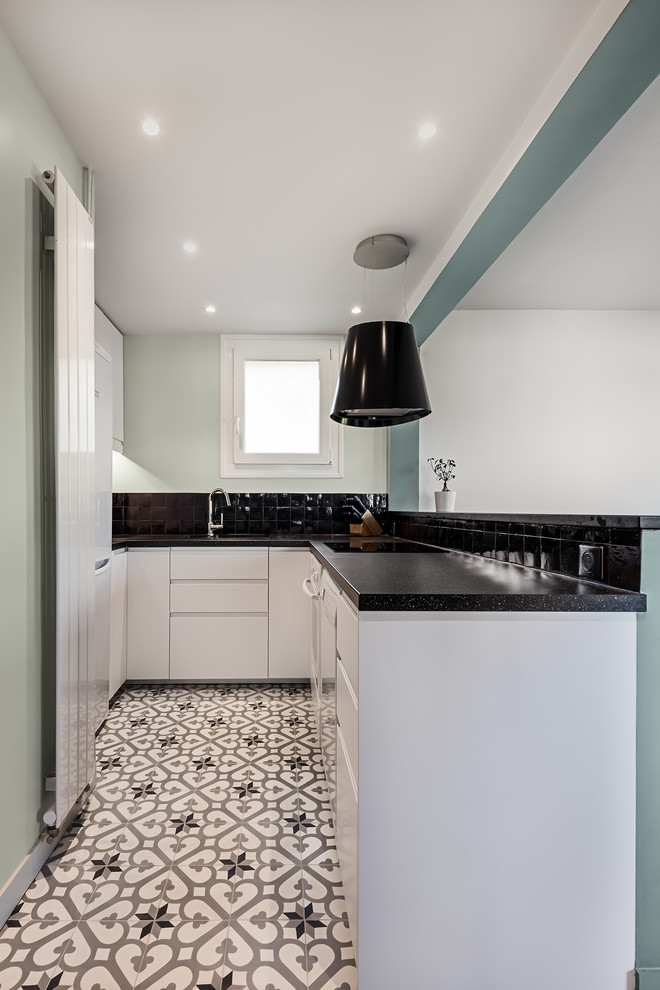 This is an example of a small contemporary l-shaped open plan kitchen in Paris with a submerged sink, white cabinets, granite worktops, black splashback, porcelain splashback, white appliances, cement flooring, no island, white floors and black worktops.