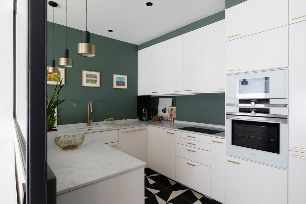 На фото: п-образная кухня среднего размера в современном стиле с одинарной мойкой, белыми фасадами, зеленым фартуком, белой техникой, полом из керамогранита, черным полом и белой столешницей