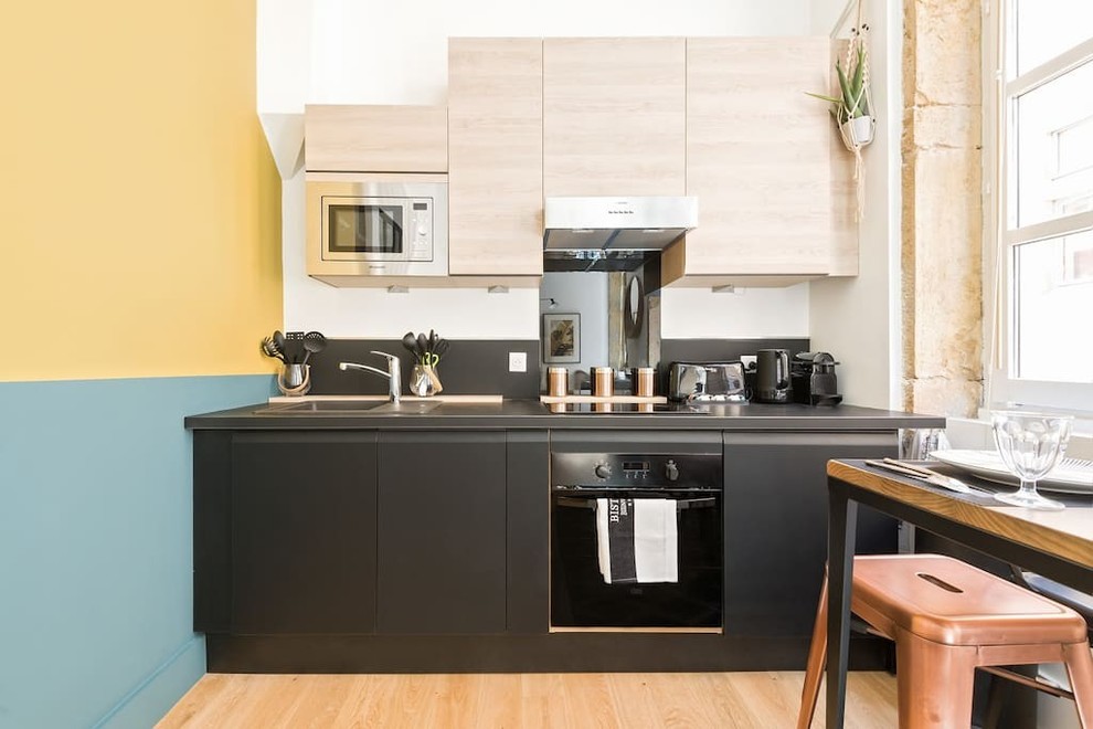 Exemple d'une cuisine linéaire scandinave avec un évier 1 bac, un placard à porte plane, des portes de placard noires, une crédence noire, un électroménager noir, parquet clair et une crédence en feuille de verre.