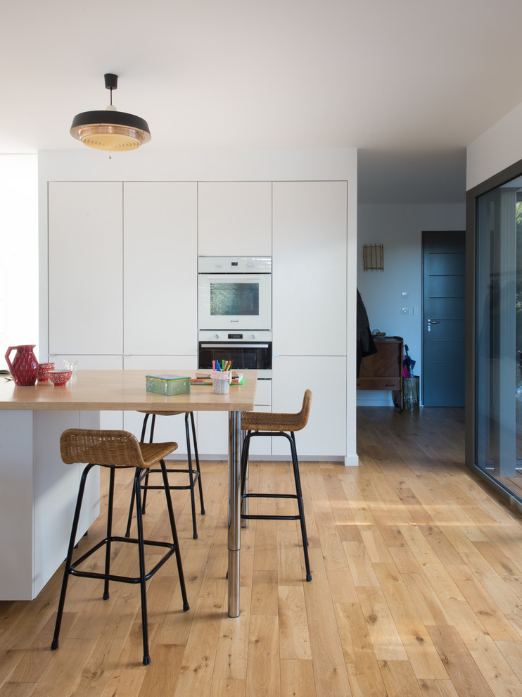 Moderne Küche mit flächenbündigen Schrankfronten, weißen Schränken, weißen Elektrogeräten, hellem Holzboden und Kücheninsel in Montpellier