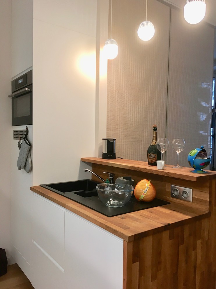 Foto di una piccola cucina minimal con ante a filo, ante bianche, top in legno, paraspruzzi blu, elettrodomestici da incasso, pavimento in legno massello medio e top marrone