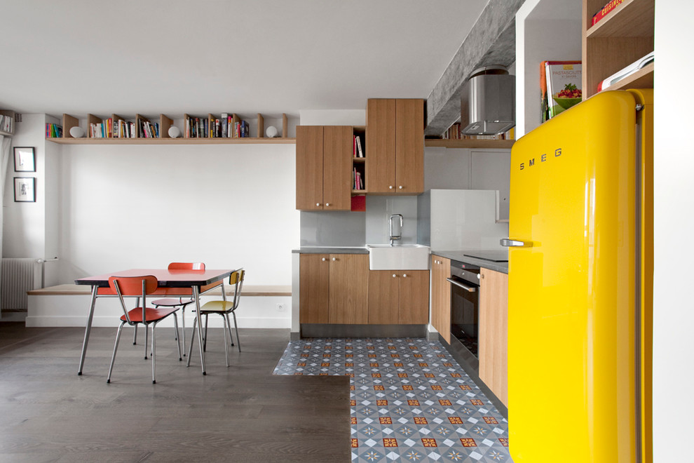 Mittelgroße Moderne Wohnküche in L-Form mit Landhausspüle, hellbraunen Holzschränken, Küchenrückwand in Grau, Glasrückwand, Elektrogeräten mit Frontblende und Keramikboden in Paris