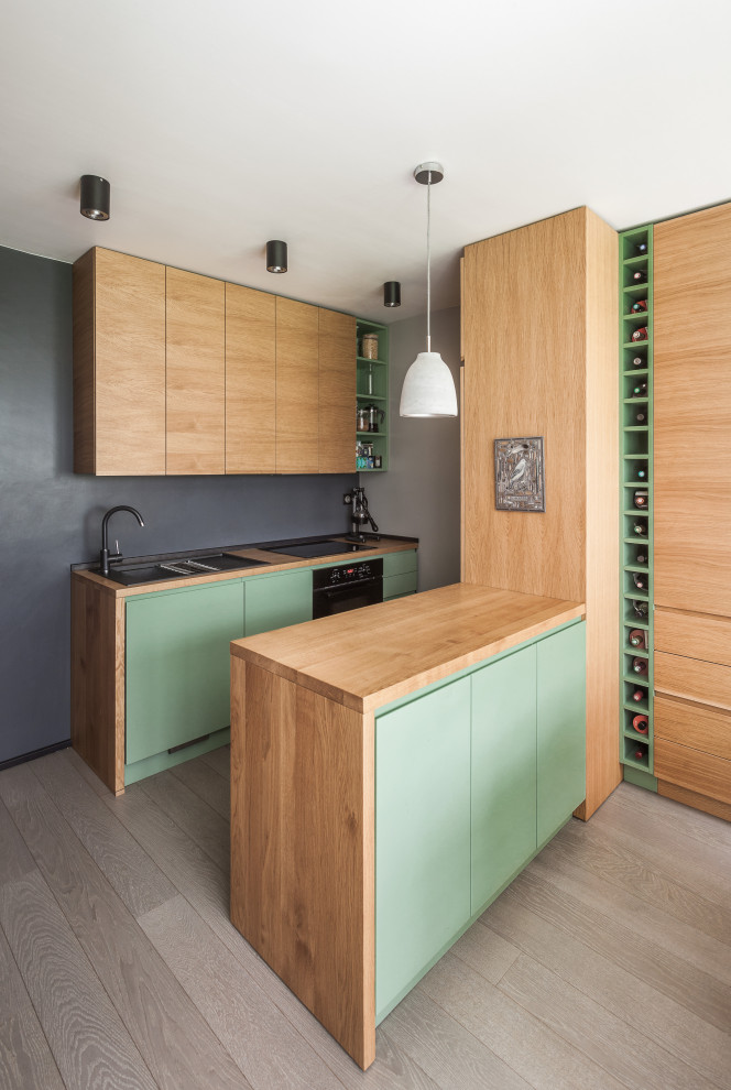 Cette photo montre une petite cuisine américaine parallèle et encastrable scandinave en bois clair avec un évier 1 bac, un placard à porte affleurante, un plan de travail en bois, une crédence noire, parquet peint et un sol gris.