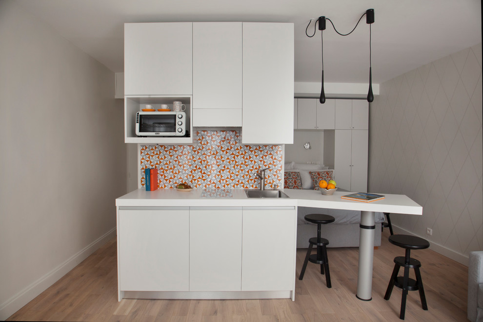 Inspiration for a small contemporary galley kitchen/diner in Paris with an integrated sink, flat-panel cabinets, laminate countertops, multi-coloured splashback, terracotta splashback, integrated appliances, light hardwood flooring, an island, white cabinets, beige floors and white worktops.
