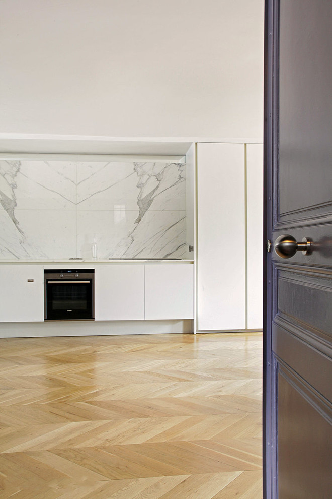 Bild på ett mellanstort funkis linjärt kök med öppen planlösning, med en integrerad diskho, luckor med infälld panel, marmorbänkskiva, vitt stänkskydd, stänkskydd i sten, integrerade vitvaror och ljust trägolv