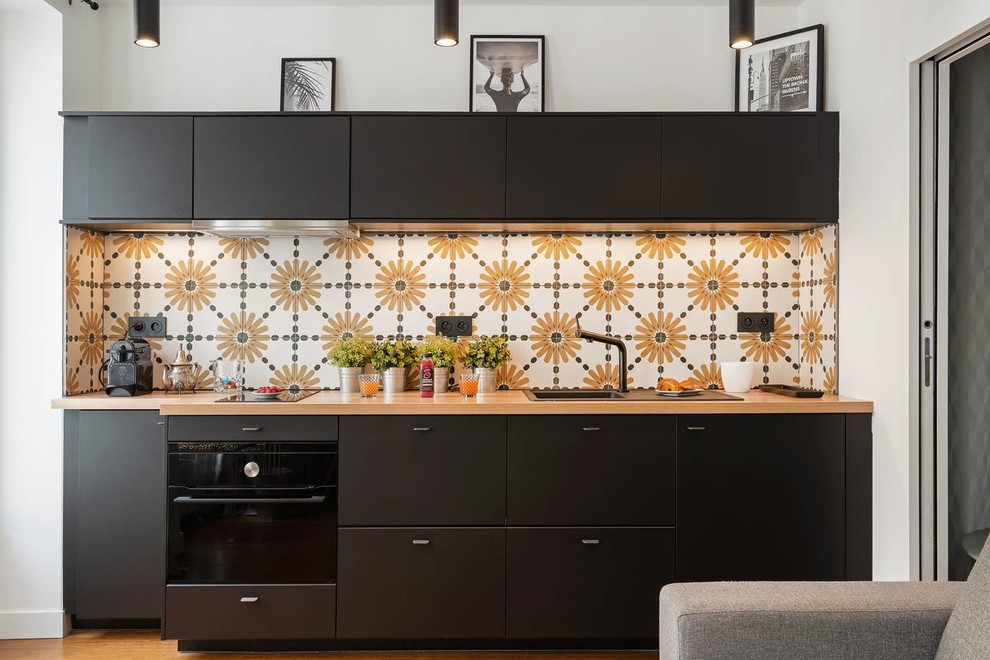 Idéer för ett mellanstort modernt brun linjärt kök med öppen planlösning, med luckor med profilerade fronter, svarta skåp, träbänkskiva, gult stänkskydd, stänkskydd i cementkakel, svarta vitvaror, ljust trägolv och brunt golv