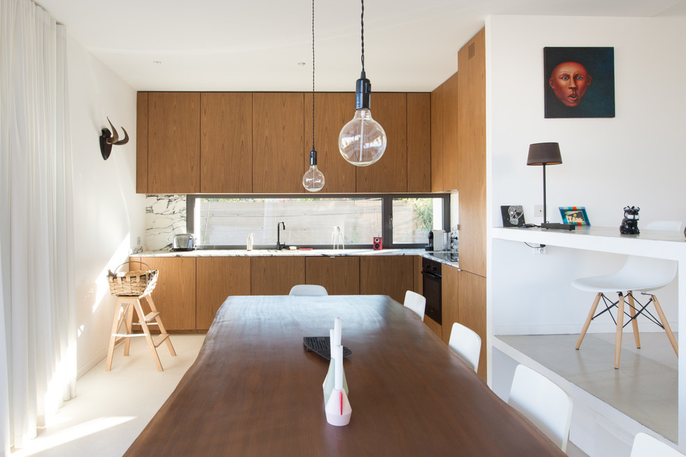 Moderne Wohnküche ohne Insel in L-Form mit flächenbündigen Schrankfronten, hellbraunen Holzschränken, Rückwand aus Stein und schwarzen Elektrogeräten in Montpellier