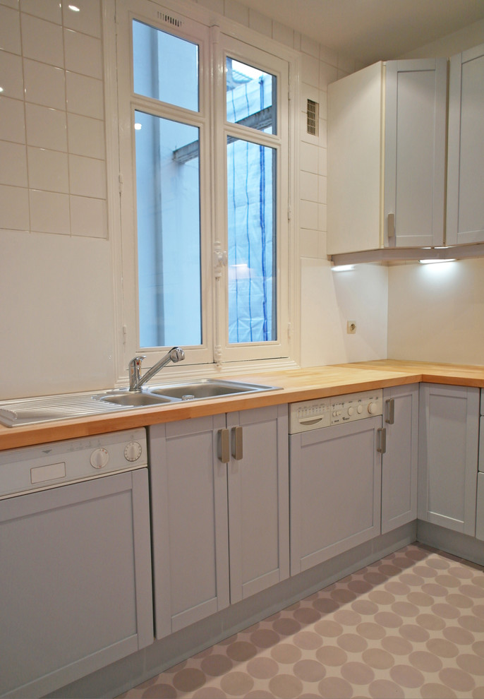 This is an example of a medium sized retro l-shaped enclosed kitchen in Paris with a submerged sink, flat-panel cabinets, grey cabinets, wood worktops, white splashback, vinyl flooring and no island.