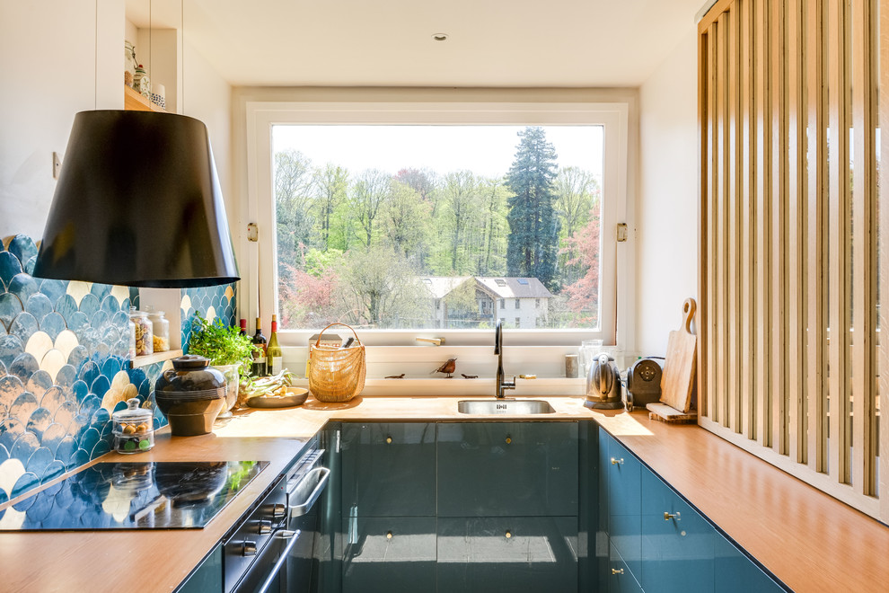 Small contemporary u-shaped kitchen in Paris with a single-bowl sink, flat-panel cabinets, blue cabinets, wood worktops and multi-coloured splashback.