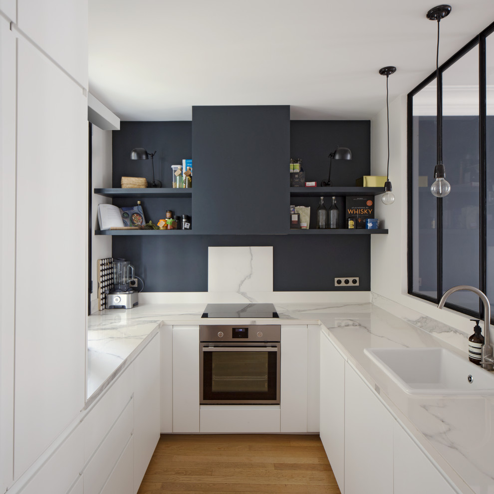Geschlossene Moderne Küche in U-Form mit Einbauwaschbecken, flächenbündigen Schrankfronten, weißen Schränken, Küchengeräten aus Edelstahl, braunem Holzboden und braunem Boden in Paris