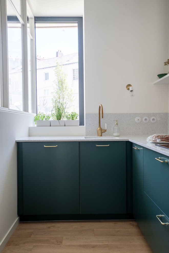 World-inspired l-shaped kitchen in Nantes with a single-bowl sink, flat-panel cabinets, green cabinets, light hardwood flooring, beige floors and grey worktops.