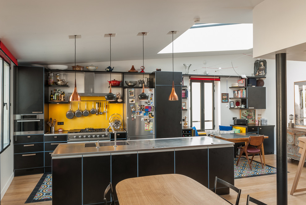 Diseño de cocina ecléctica grande abierta con puertas de armario negras, una isla, fregadero integrado, salpicadero amarillo, electrodomésticos negros y encimeras grises