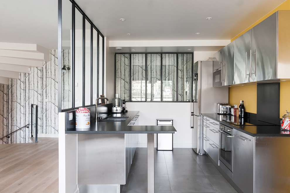 Photo of a medium sized scandinavian galley enclosed kitchen in Paris with a submerged sink, flat-panel cabinets, stainless steel cabinets, stainless steel appliances, a breakfast bar, ceramic flooring and a feature wall.