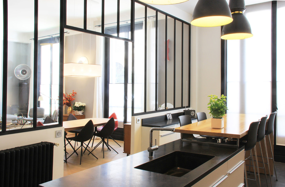 Photo of a large contemporary single-wall open plan kitchen in Paris with an integrated sink, flat-panel cabinets, light wood cabinets, marble worktops, white splashback, marble splashback, stainless steel appliances, lino flooring, an island and black floors.