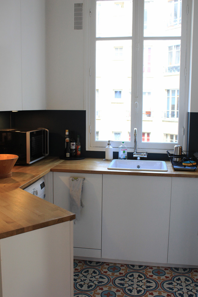 На фото: маленькая п-образная кухня-гостиная в современном стиле с одинарной мойкой, белыми фасадами, деревянной столешницей, синим фартуком, полом из цементной плитки и разноцветным полом без острова для на участке и в саду