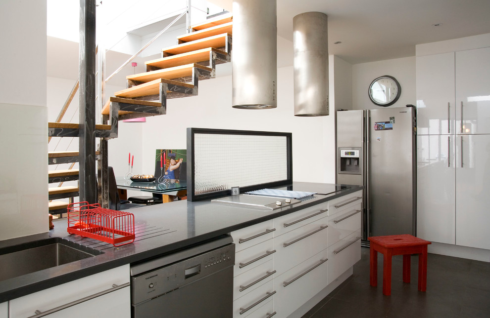 Immagine di una cucina industriale di medie dimensioni con lavello sottopiano, ante lisce, ante bianche, paraspruzzi con lastra di vetro, elettrodomestici in acciaio inossidabile e pavimento in cemento