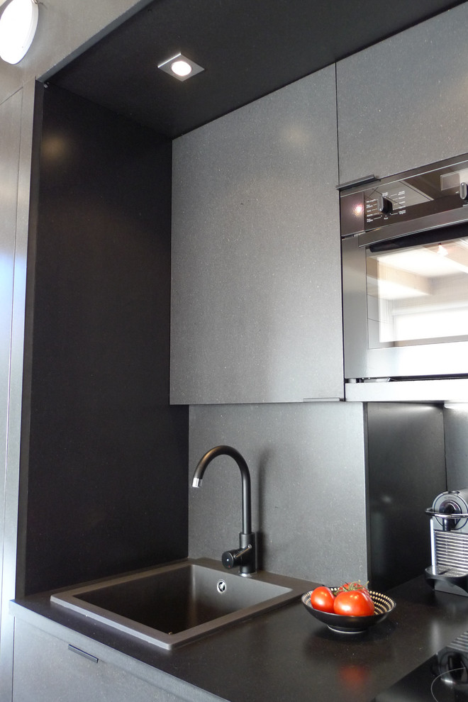 Bild på ett litet funkis linjärt kök med öppen planlösning, med en enkel diskho, luckor med profilerade fronter, svarta skåp, träbänkskiva, svart stänkskydd, svarta vitvaror och klinkergolv i keramik