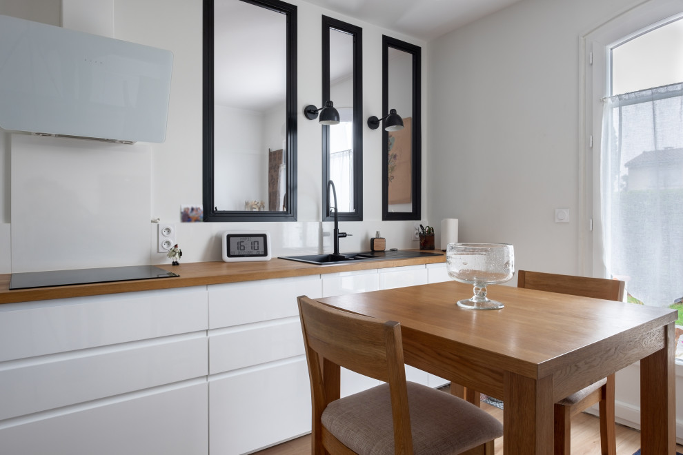 Design ideas for a contemporary galley enclosed kitchen in Toulouse with a single-bowl sink, flat-panel cabinets, wood worktops, white splashback, window splashback, integrated appliances, vinyl flooring, beige floors and brown worktops.