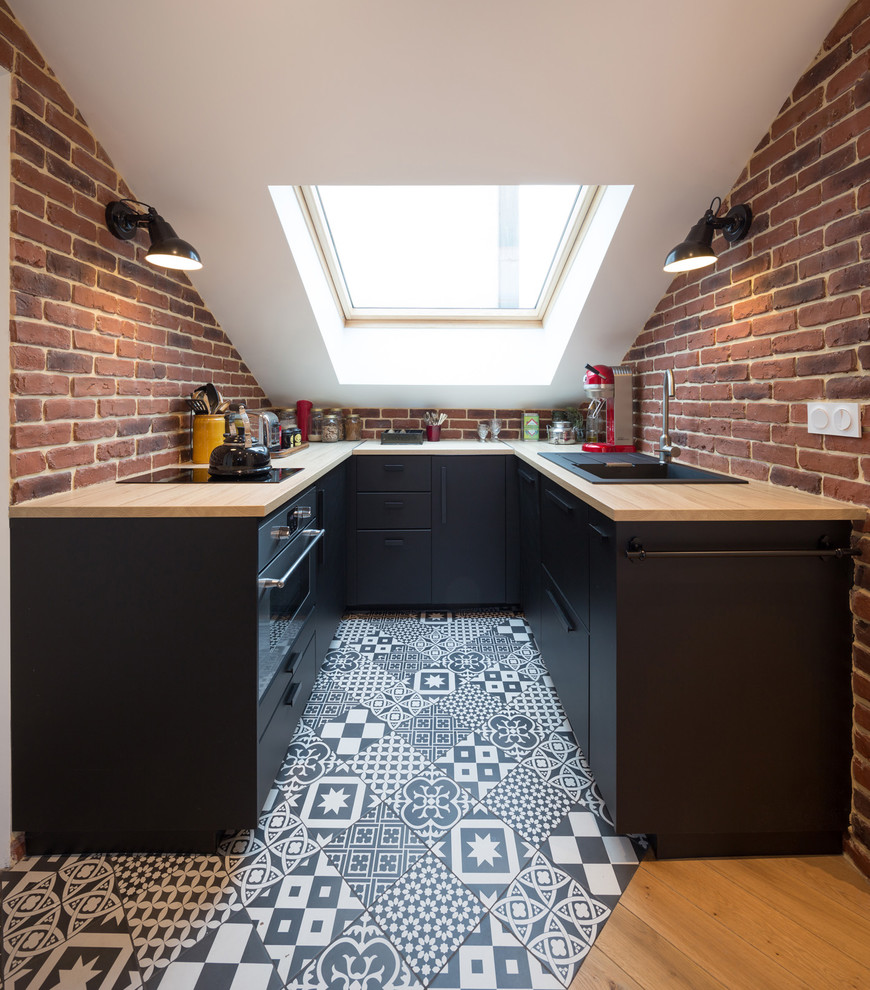 Example of a danish cement tile floor and multicolored floor eat-in kitchen design in Paris with a drop-in sink, flat-panel cabinets, black cabinets, wood countertops, red backsplash, brick backsplash, black appliances and brown countertops
