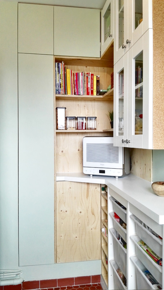 Small midcentury l-shaped enclosed kitchen in Paris with a belfast sink, glass-front cabinets, white cabinets, laminate countertops, green splashback, cement tile splashback, stainless steel appliances, terracotta flooring, no island and red floors.