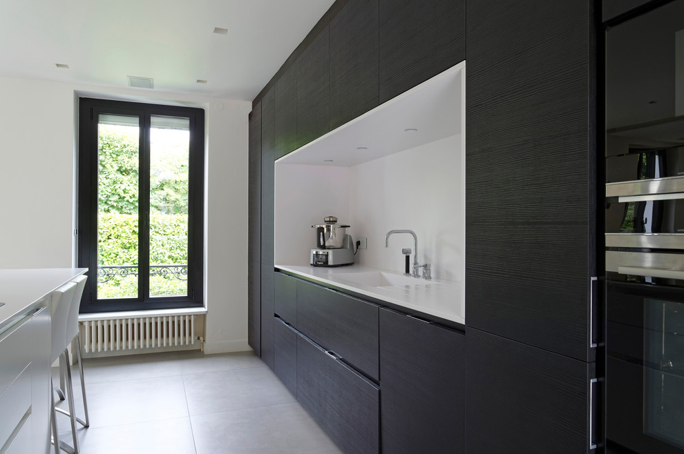 Photo of a modern kitchen/diner in Paris with a submerged sink, recessed-panel cabinets, dark wood cabinets, engineered stone countertops, white splashback, stainless steel appliances, ceramic flooring, an island and white floors.