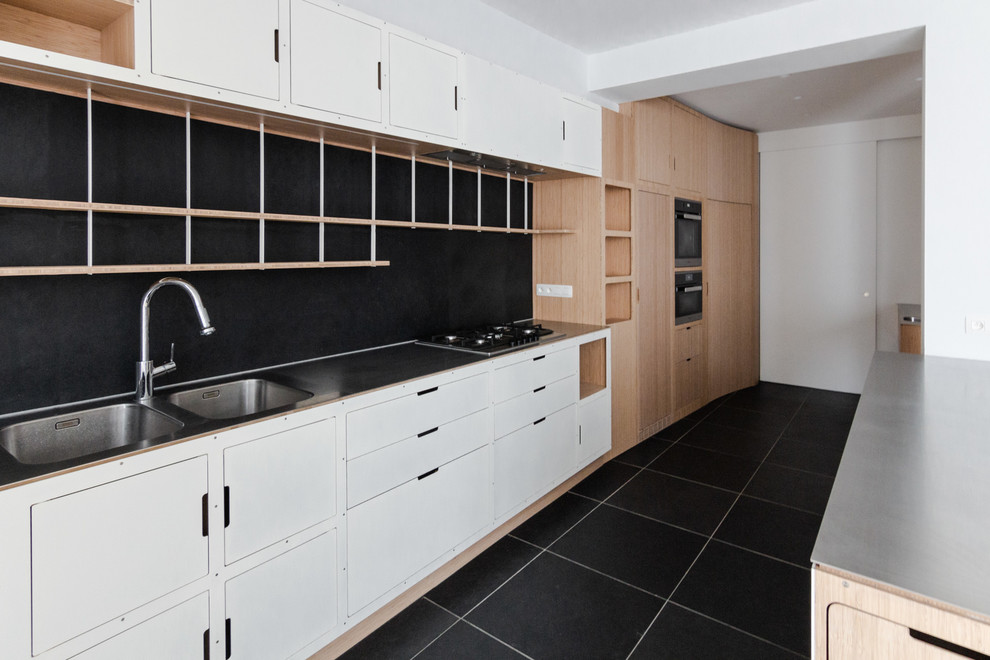 Foto på ett mycket stort minimalistiskt kök, med en integrerad diskho, luckor med profilerade fronter, skåp i ljust trä, bänkskiva i rostfritt stål, svart stänkskydd, stänkskydd i skiffer, integrerade vitvaror, skiffergolv, en köksö och svart golv
