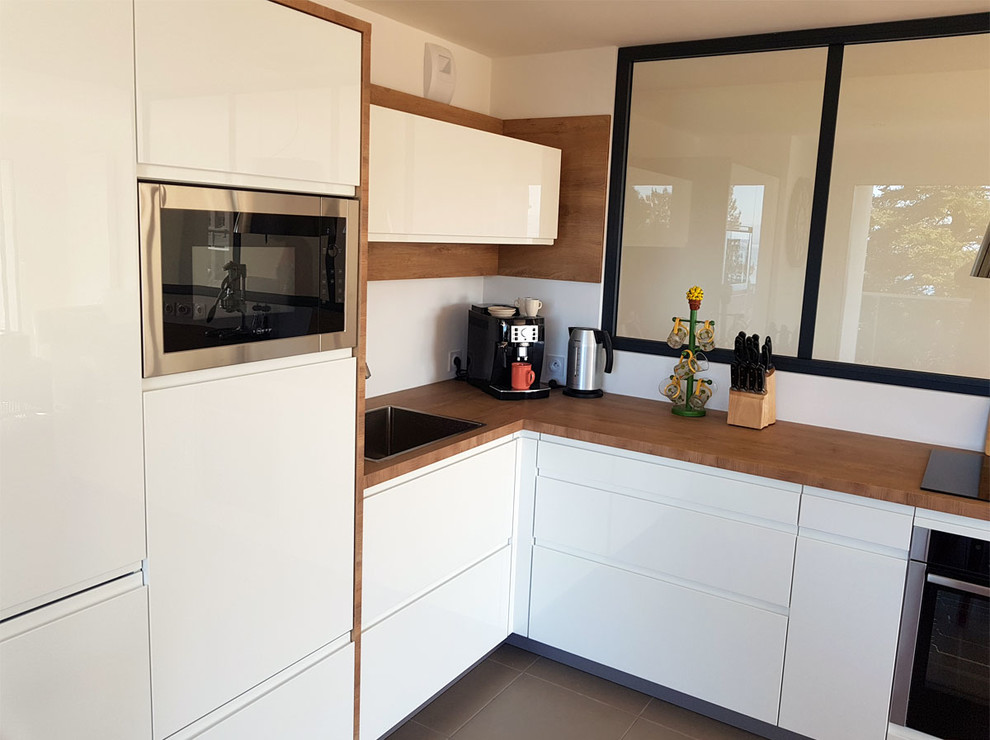 This is an example of a medium sized modern l-shaped kitchen/diner in Other with a submerged sink, white cabinets, wood worktops, stainless steel appliances, ceramic flooring, no island, brown floors and brown worktops.