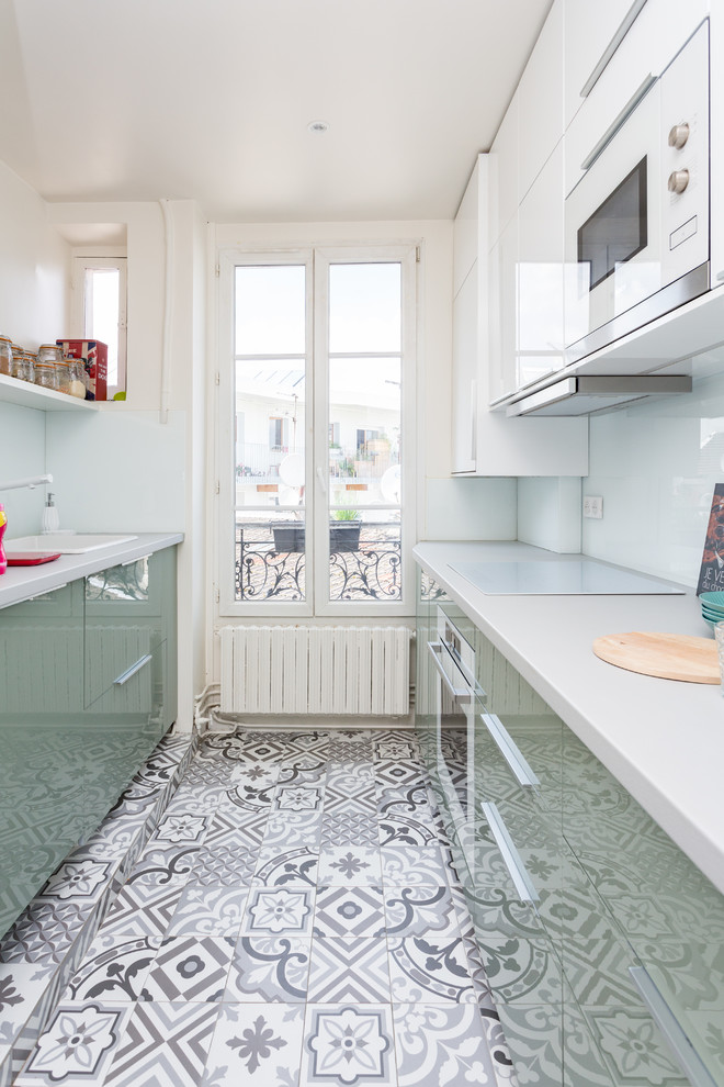 パリにあるコンテンポラリースタイルのおしゃれなキッチン (ドロップインシンク、フラットパネル扉のキャビネット、緑のキャビネット、白い調理設備、アイランドなし、マルチカラーの床、白いキッチンカウンター) の写真