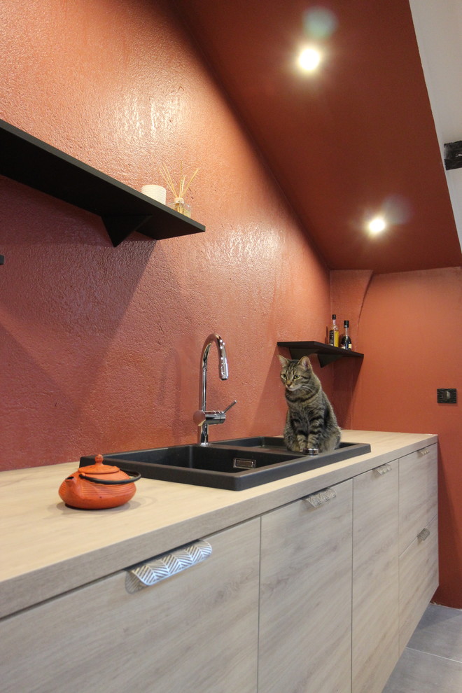 Immagine di una cucina design di medie dimensioni con lavello sottopiano, ante a filo, ante in legno chiaro, top in laminato, paraspruzzi rosso, elettrodomestici da incasso, pavimento con piastrelle in ceramica, pavimento grigio e top nero